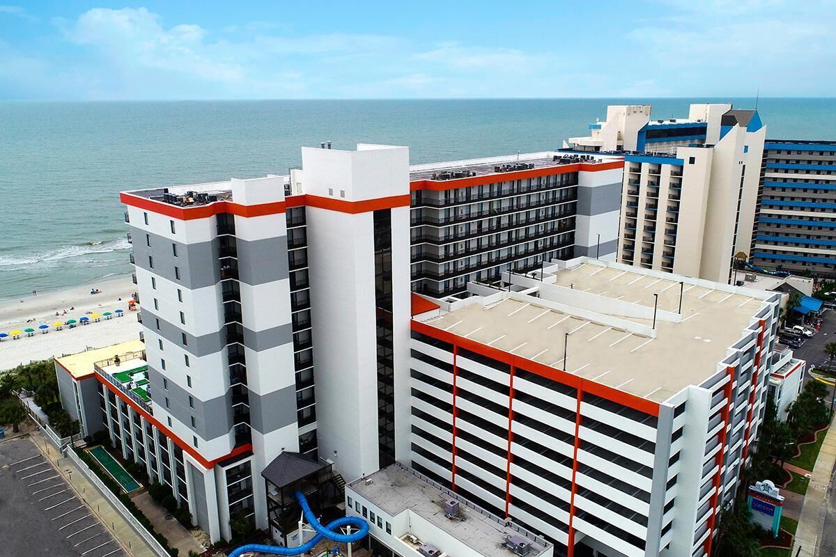 A multi-story hotel with a rooftop pool, adjacent to a beach.