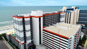 A multi-story hotel with a rooftop pool, adjacent to a beach.