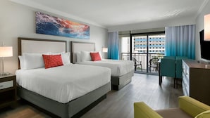 Habitación de hotel con dos camas, un escritorio, una silla, un televisor y un balcón con vista a un edificio.