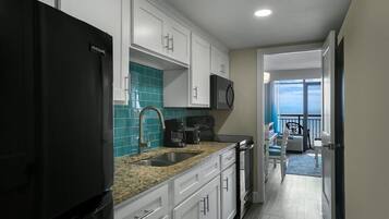 A modern kitchen with white cabinets, a black refrigerator, a microwave, and a coffee maker. There is a view of a balcony with a chair and a table.