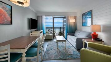 A hotel room with a balcony, a dining area, a sofa, a TV, and a lamp.