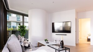 A modern living room with a sofa, a glass coffee table, a flat-screen TV, and a balcony with a view of buildings. - The Ritz + Parking & Amenities (Melbourne)