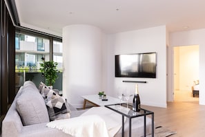 Un salon moderne avec un canapé, une table basse en verre, un téléviseur à écran plat et un balcon offrant une vue sur les immebles.