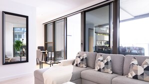 A modern living room with a grey sofa, a white coffee table, and a large window with a view of the city. - The Ritz + Parking & Amenities (Melbourne)