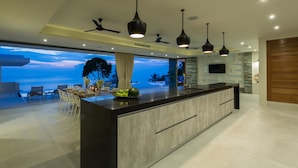 Una cocina moderna con una isla grande, iluminación colgante y vistas al océano.