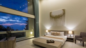 Una habitación de hotel moderna con una cama grande, mesitas de noche, una silla, un ventanal con vistas y un cuadro en la pared.