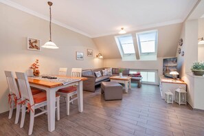 Amplia sala de estar con una mesa de comedor, sofá y reposapiés, techo alto y tragaluz.