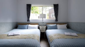 A hotel room with two beds, a nightstand with a lamp, and a window with curtains.