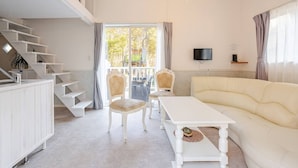 A modern living room with a white sofa, a dining table, and a staircase leading to an upper level.