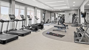 Une salle de sport moderne équipée de tapis de course, de vélos elliptiques, de bancs de musculation et de poids libres.