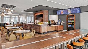 Un hall d’hôtel moderne doté d’un long comptoir d’accueil, de plusieurs espaces salon, d’un bar et d’un distributeur automatique de boissons.