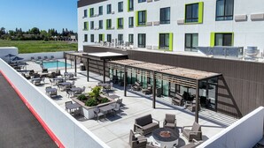 Une terrasse sur le toit avec des espaces de détente en plein air, une piscine et un bâtiment moderne doté de grandes fenêtres et de touches de verdure.