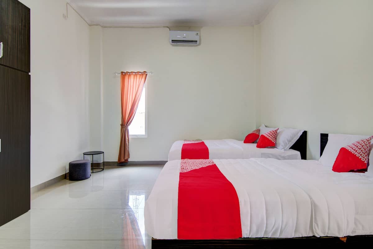 A hotel room with two beds, a wardrobe, a small table, and a window with curtains.