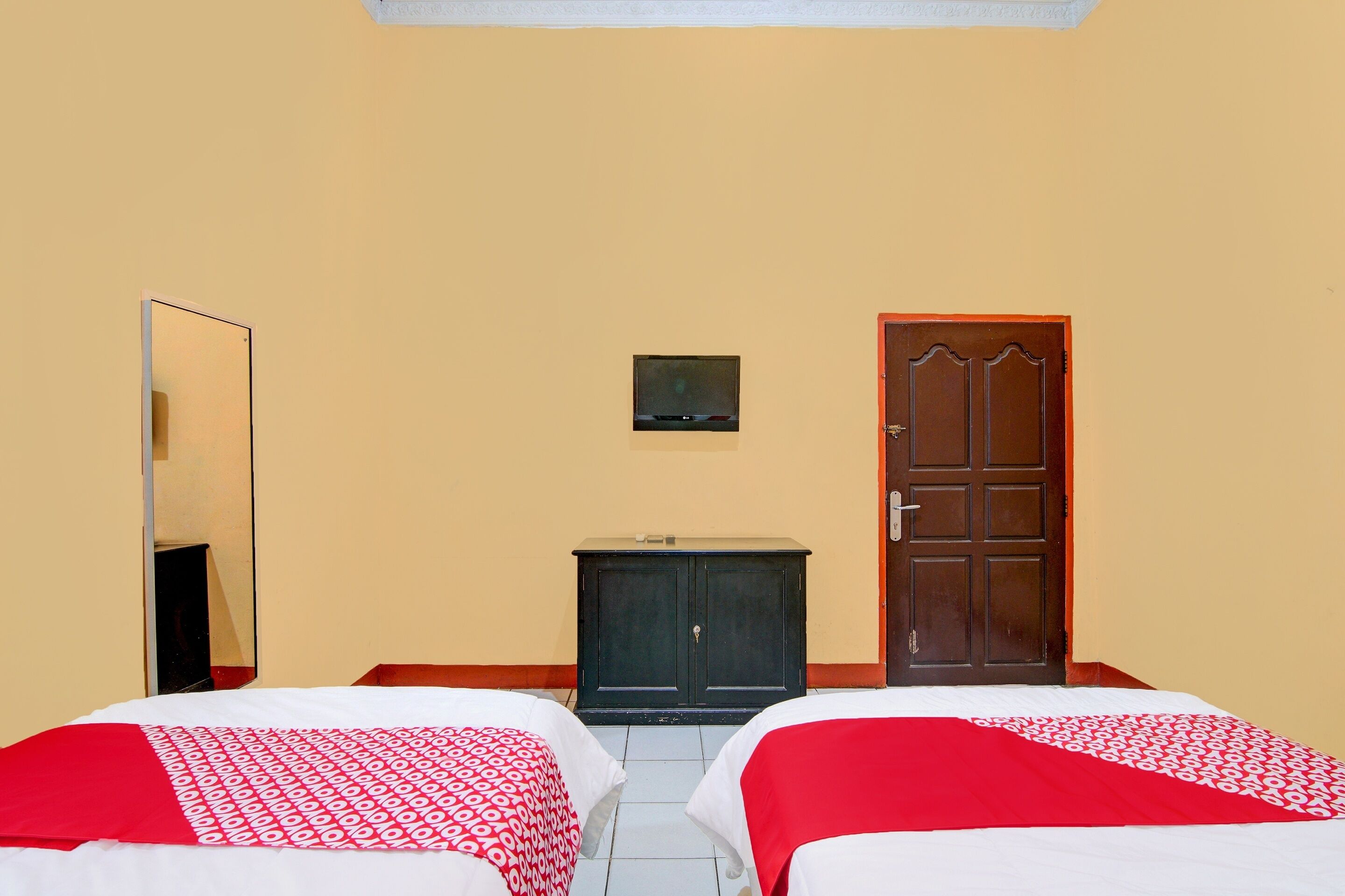 A hotel room with two beds, a wardrobe, a television, and a door.
