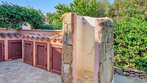 A stone-walled shower enclosure with a tiled floor, surrounded by a tiled roof and a stone wall.
