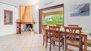 A dining area with a table and chairs, a fireplace, and a view of greenery outside.