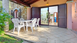 Eine Terrasse im Freien mit einer Steinwand, einem Tisch mit Stühlen und einer Glastür, die in einen Innenraum führt.