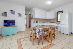 A modern kitchen with white cabinets, a dining table with chairs, a refrigerator, and a television on a cabinet. - Villa "Rattali 2" with Private Terrace (san teodoro)