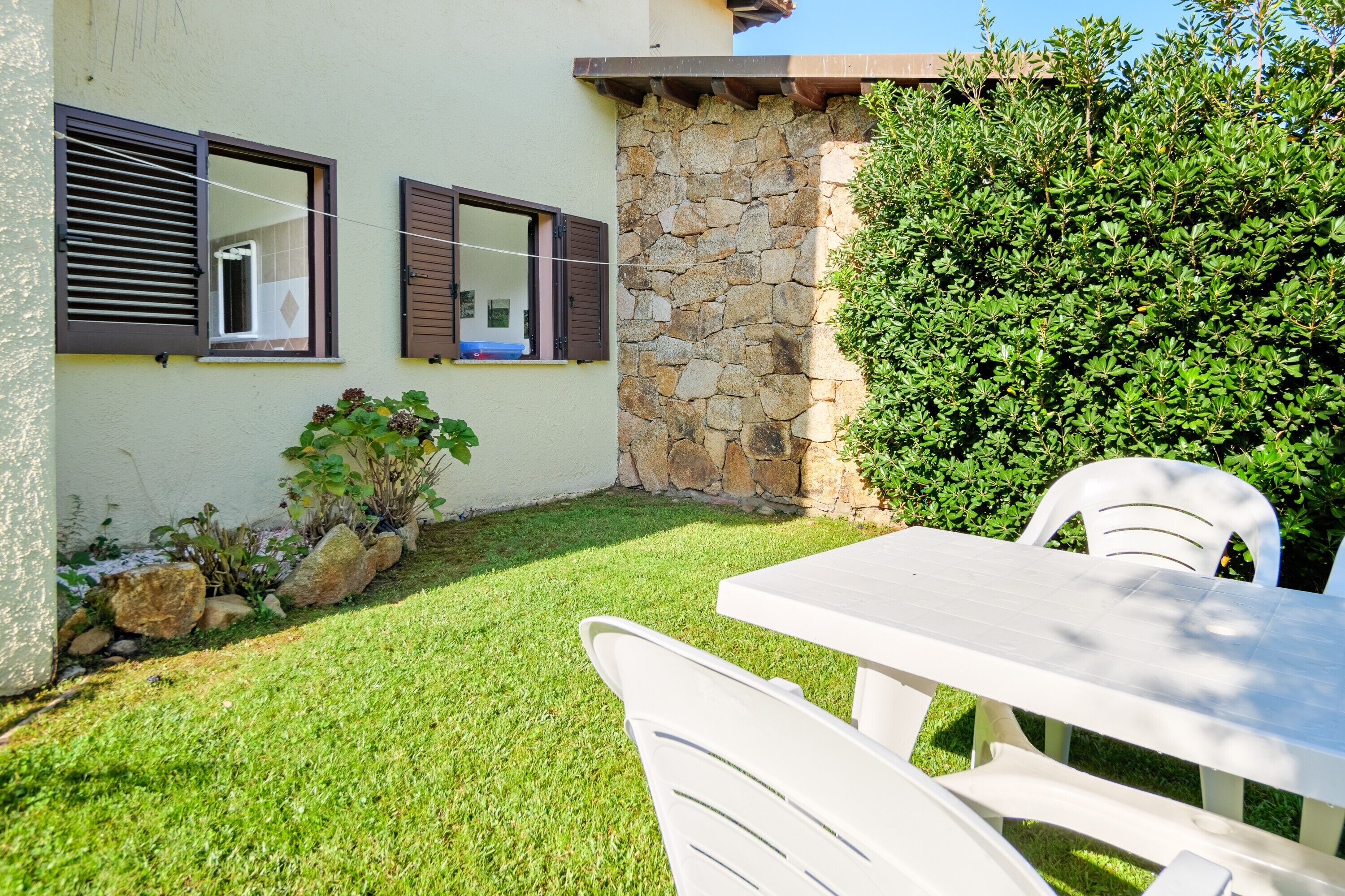 A patio with a table and chairs, a stone wall, and a well-maintained lawn.