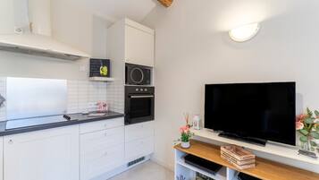Una cocina moderna con armarios blancos, microondas, horno y un televisor de pantalla plana en un estante de madera.