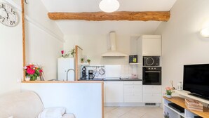 Un ambiente compatto con angolo cottura, divano, televisore e trave in legno al soffitto.