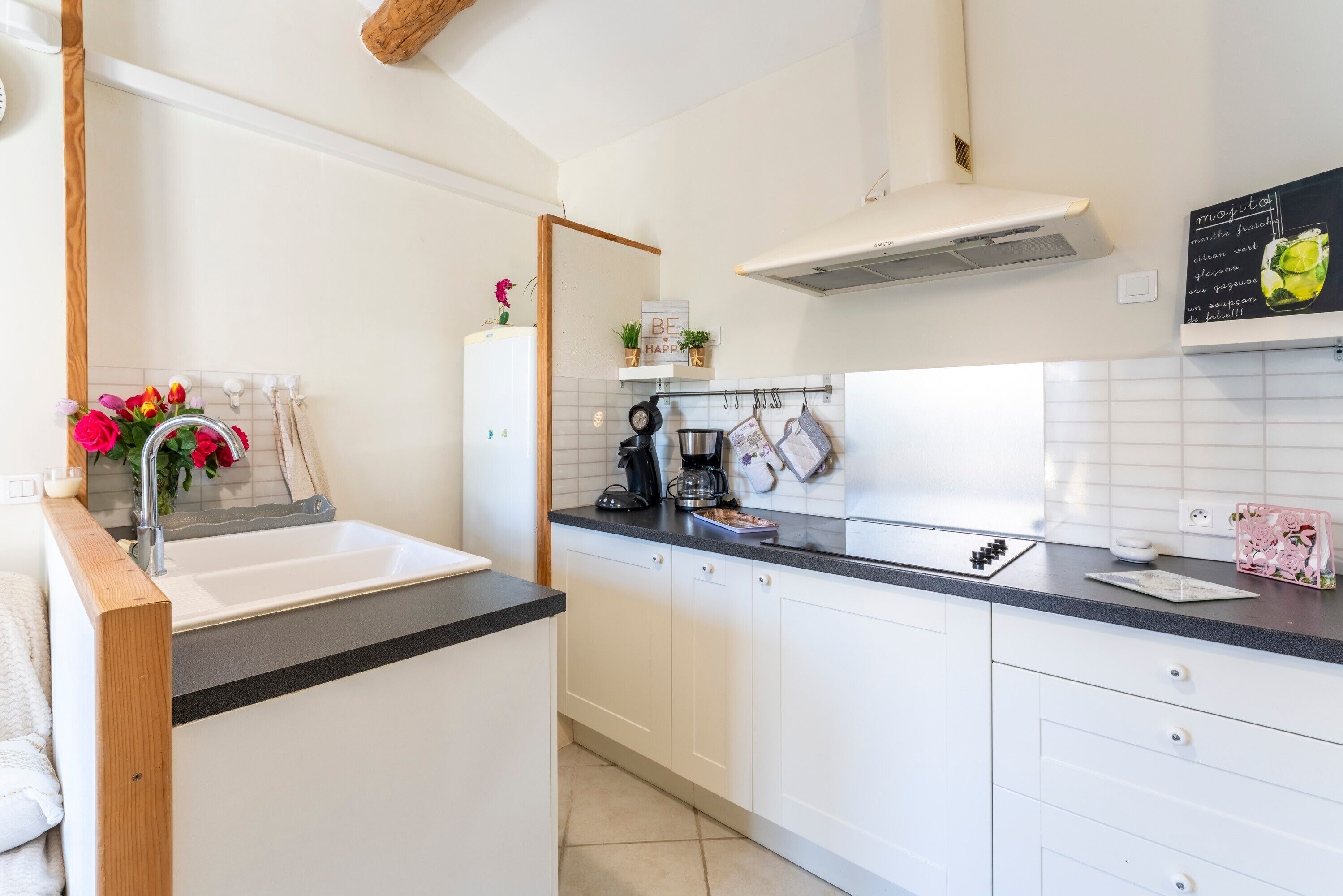 Een moderne keuken met witte kasten, een zwart aanrecht, een koffiezetapparaat en een prikbordmenu.