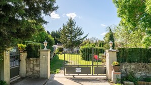 Un cancello con un vialetto che conduce a una zona residenziale, circondata da vegetazione e un cielo sereno.