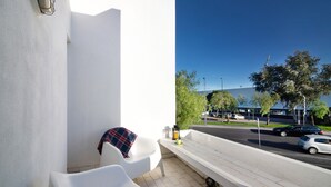 A balcony with white chairs, a bench, and a view of a road with cars.