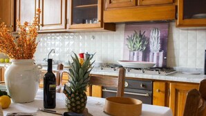 Une cuisine avec des meubles en bois, un plan de travail carrelé de carreaux blancs, une cuisinière et une table à manger recouverte d’une nappe blanche.