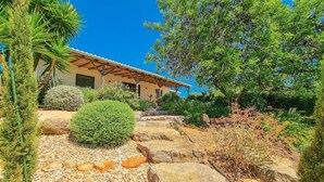Una casa con un porche cubierto, rodeada de plantas y rocas.