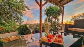 Una mesa con una copa de vino blanco, una botella de vino blanco y un plato de quesos y frutas variados.
