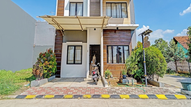 Uma casa moderna de dois andares com telhado plano, entrada coberta e uma motocicleta visível estacionada na frente.