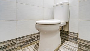 Sanitário com caixa de água e assento brancos, em frente a uma parede revestida com padrão que lembra mármore no chão.