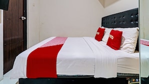 Cama bem arrumada com colcha branca e vermelha, duas almofadas vermelhas e cabeceira escura.