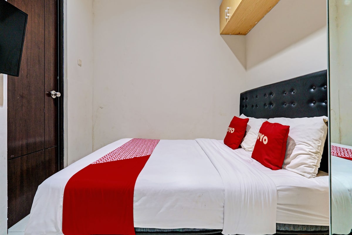 Una cama bien tendida con una colcha blanca y roja, dos almohadas rojas y un cabecero oscuro.