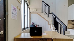 Quarto com escrivaninha de madeira, laptop, cadeira, escada com corrimão preto e janela com vista para o exterior.