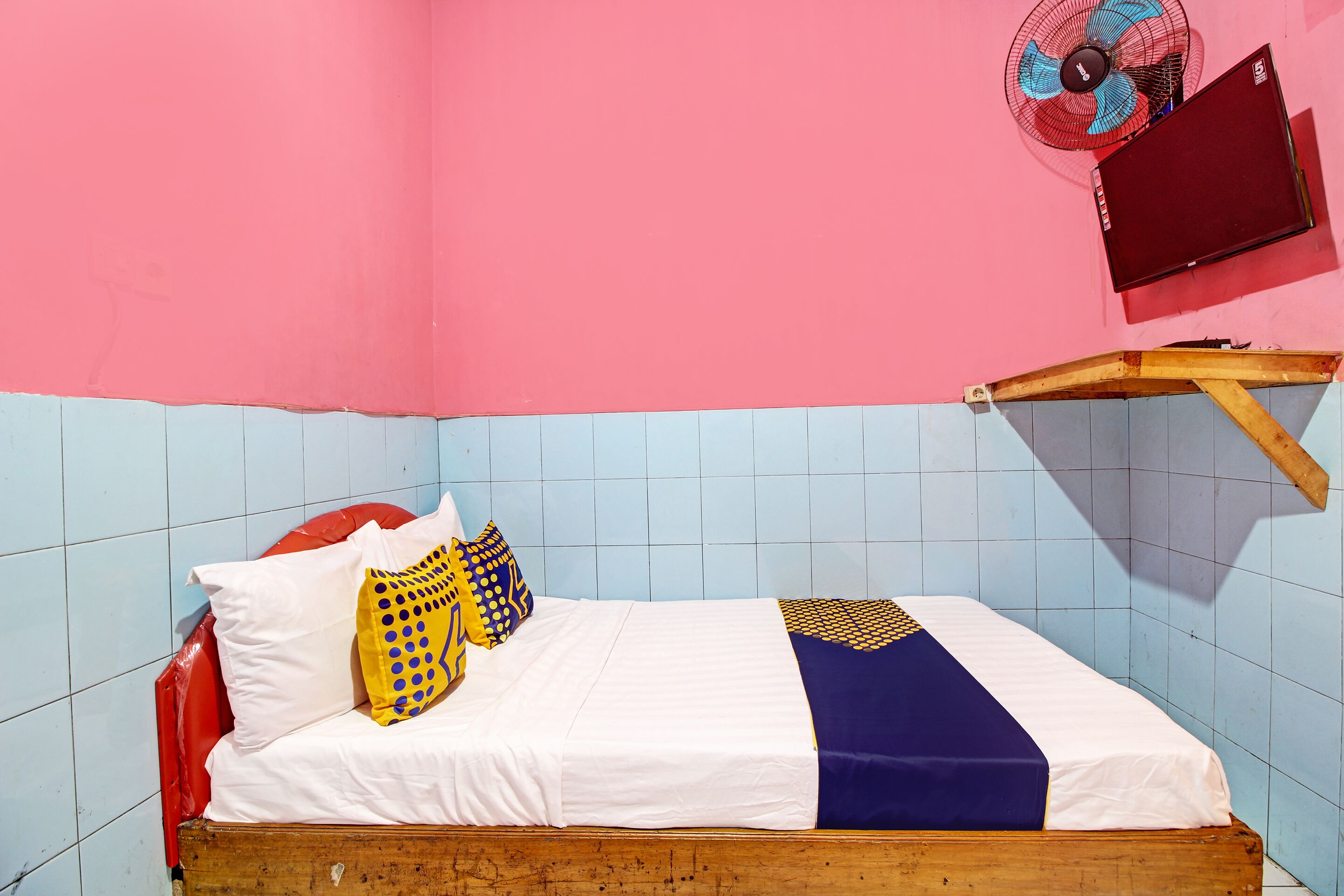 Uma cama com roupa de cama branca e azul, cabeceira vermelha e peseira de madeira.