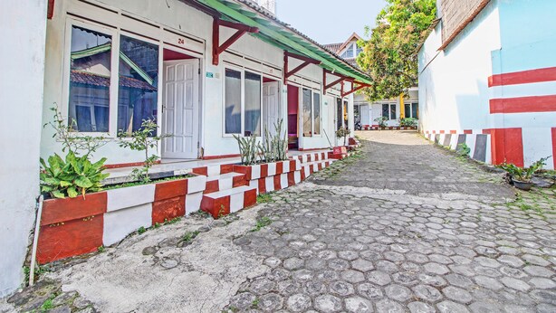 A narrow cobblestone street with buildings on either side, featuring a red and white checkered curb and potted plants along the walkway. - Hotel O 4 Saudara Hotel (Ambarawa)