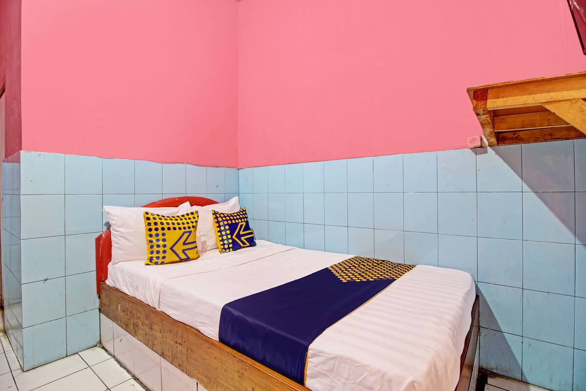 Een kleine, kleurrijke kamer met een enkel bed, een houten hoofdbord en wandtegels in blauw en roze.