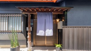 A building entrance with a wooden pergola, a sliding door, and two potted plants. - Enyu No Yado Dogo (Matsuyama)