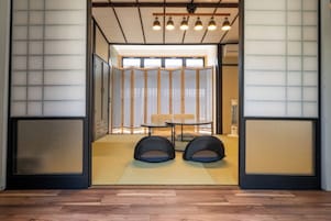 Una habitación japonesa tradicional con suelo de tatami, una mesa baja, dos cojines negros y un panel corredizo shoji.