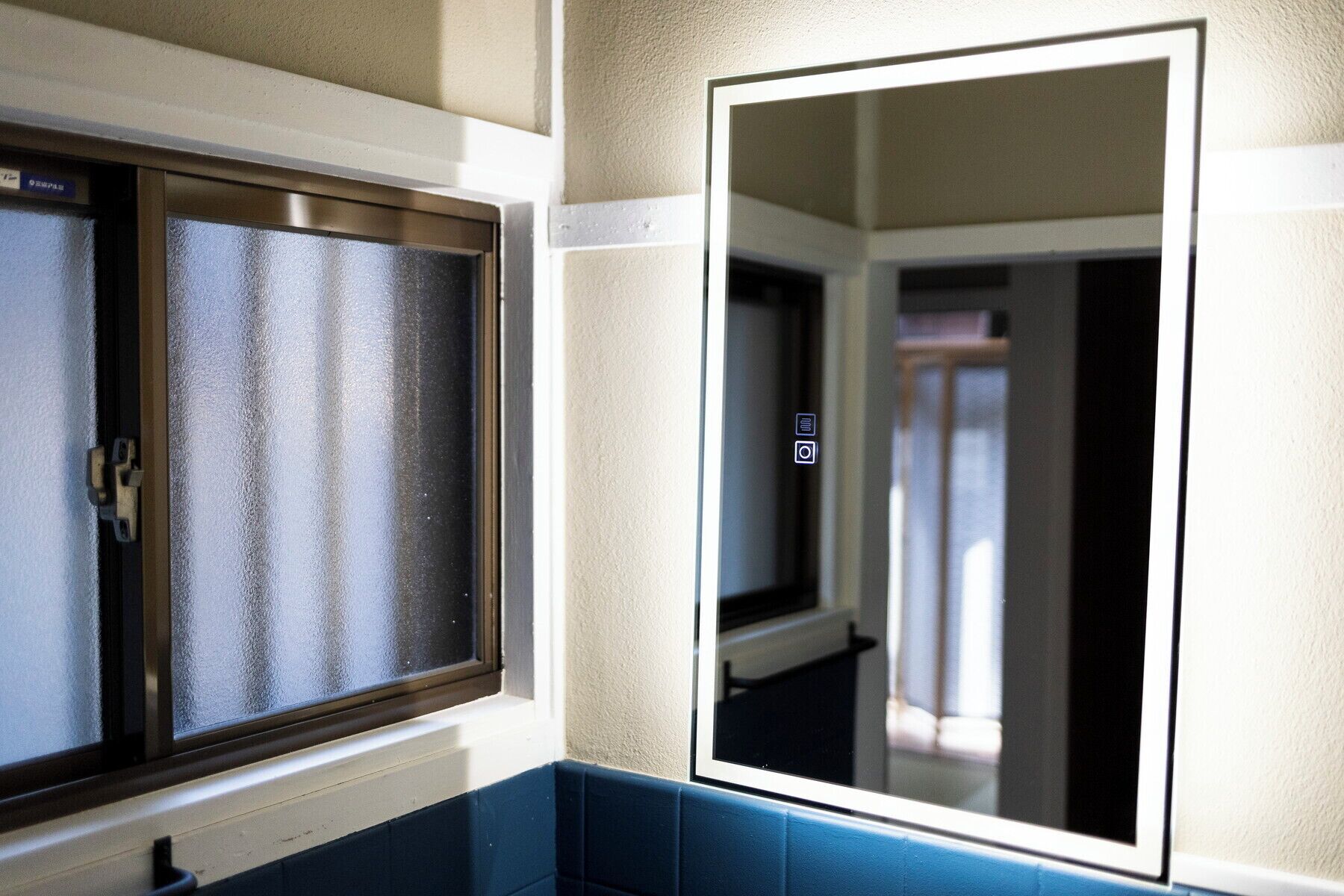 A bathroom with a frosted glass window, a mirror, and a blue tiled wall.