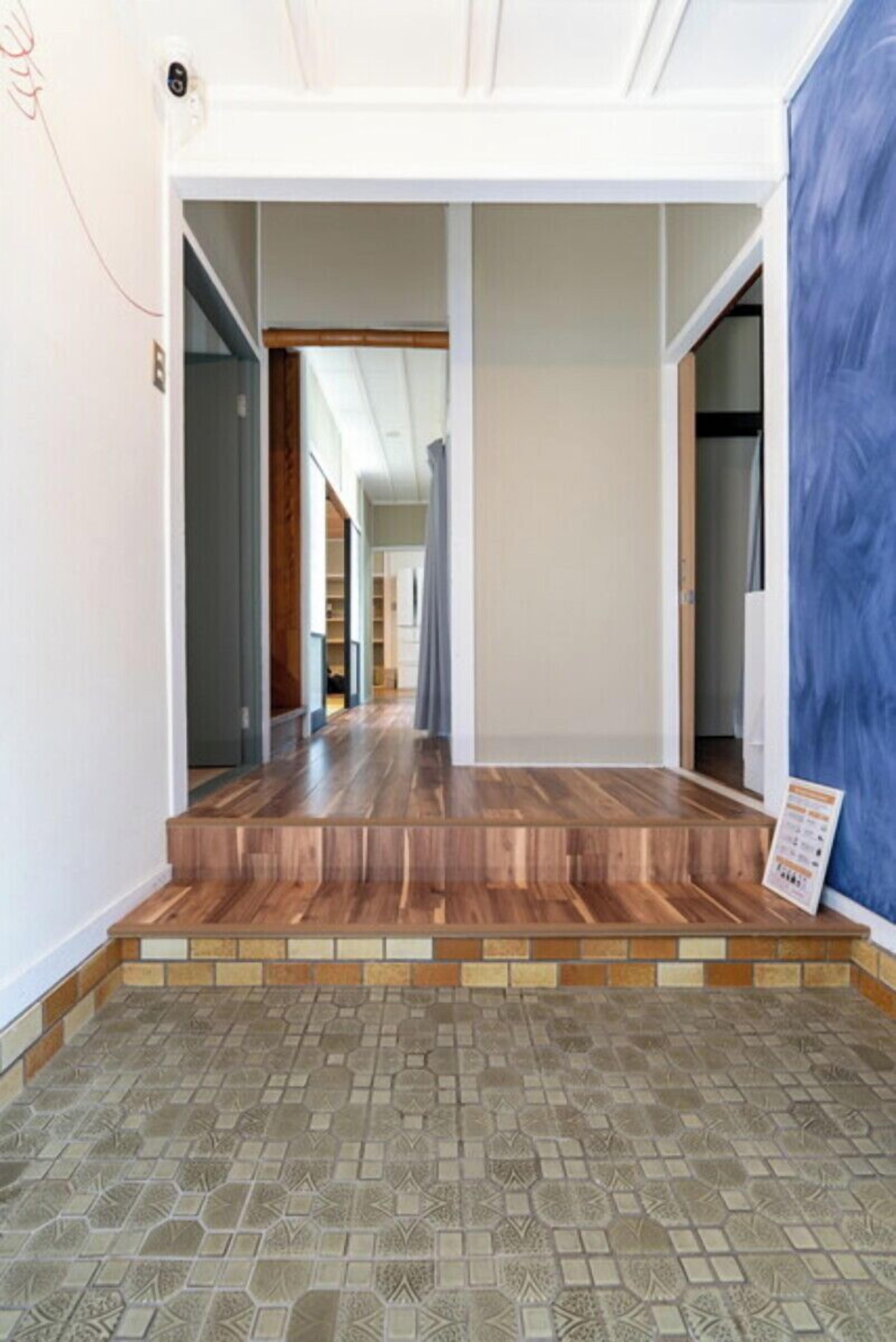 A hallway with a wooden floor, a tiled entrance, and a blue wall.