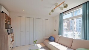 A modern living room with a sofa, a small round table, a built-in wardrobe, and a large window with curtains.