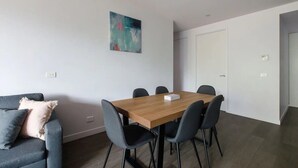 A modern room with a wooden dining table, grey chairs, a grey sofa with a cushion, and a painting on the wall.