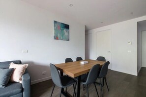 A modern room with a wooden dining table, grey chairs, a grey sofa with a cushion, and a painting on the wall.