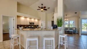 Une cuisine spacieuse avec un îlot central, des tabourets de bar blancs et un ventilateur de plafond.