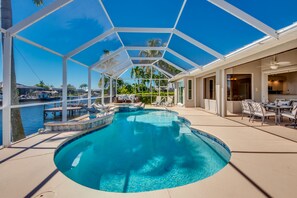 A swimming pool with a glass enclosure, lounge chairs, and a view of the water.