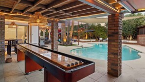 Un espace aménagé au bord de la piscine, comprenant une table de baby-foot, un barbecue et une piscine.
