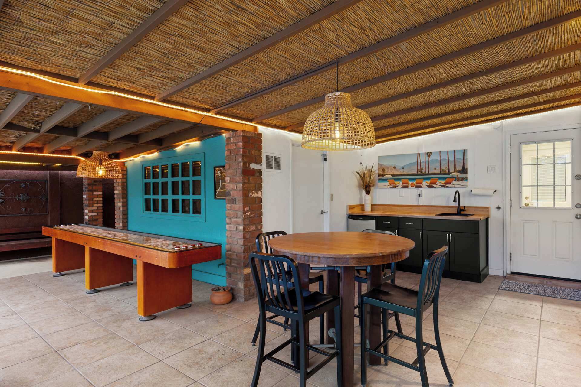 A spacious kitchen with a dining area, a blue door, and a thatched ceiling.